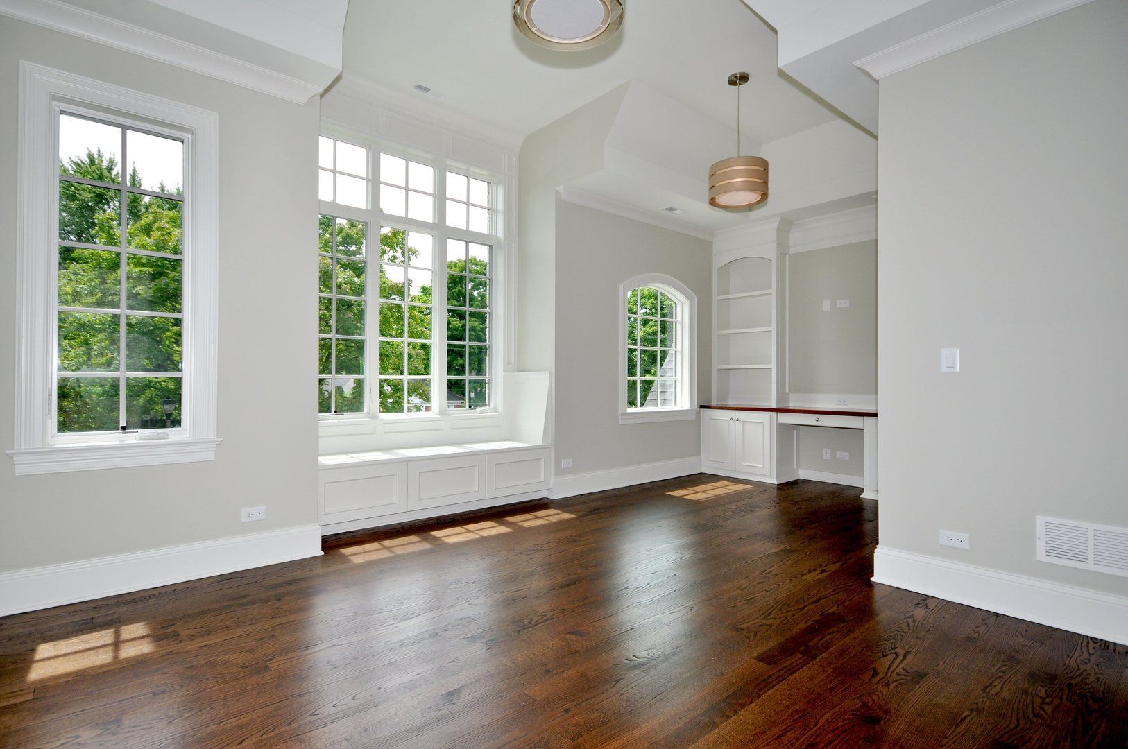 An empty living room with hardwood floors and lots of windows.