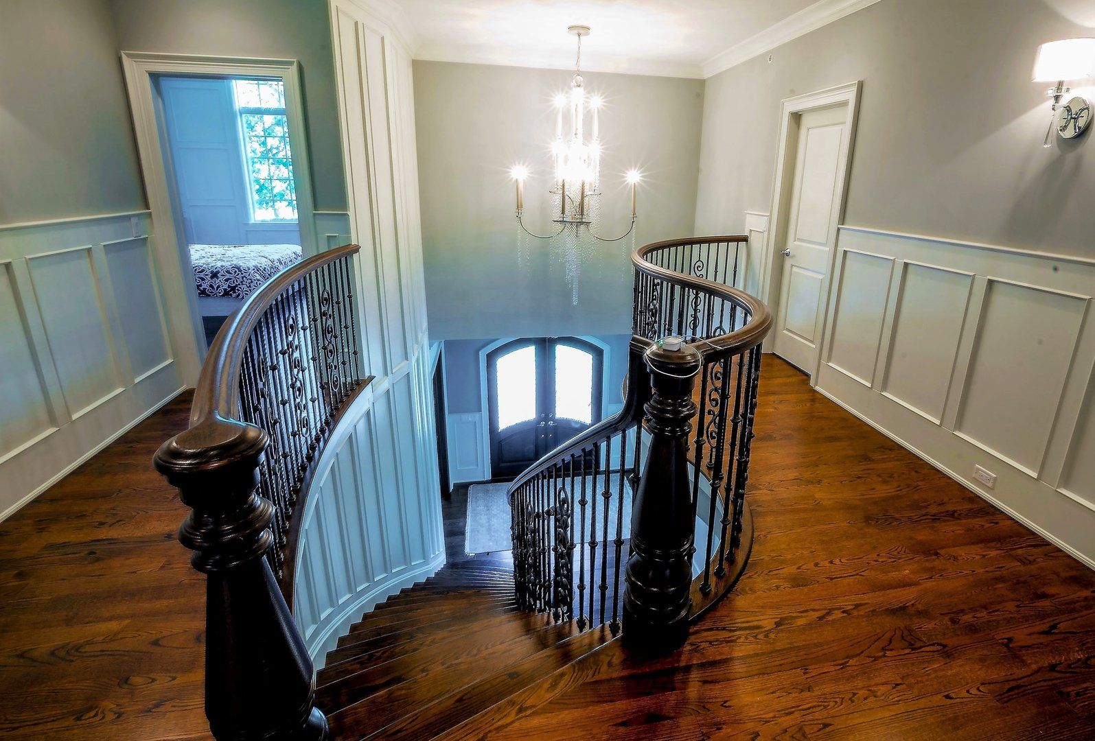 A spiral staircase in a hallway with a chandelier hanging from the ceiling.