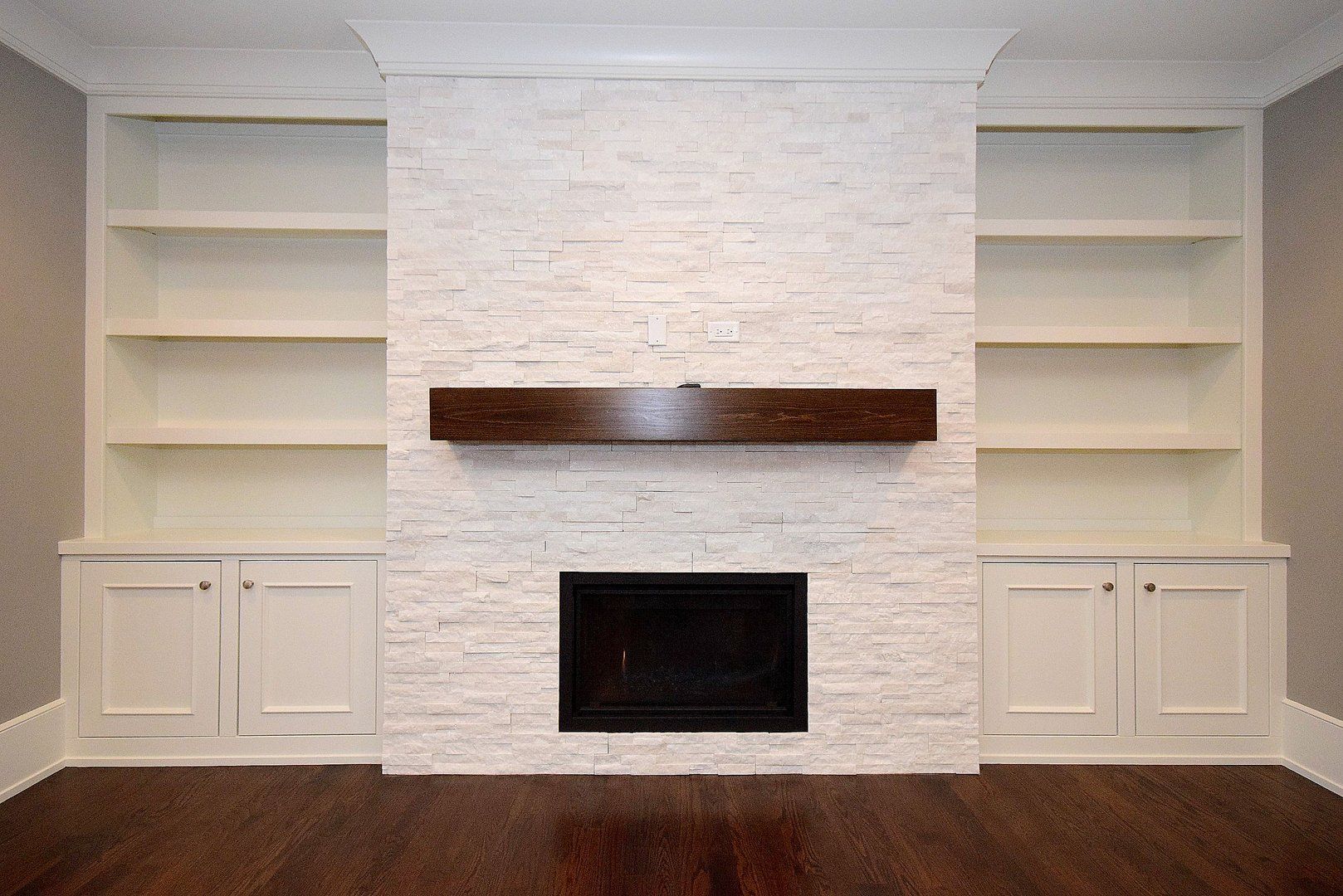 An empty living room with a fireplace and shelves