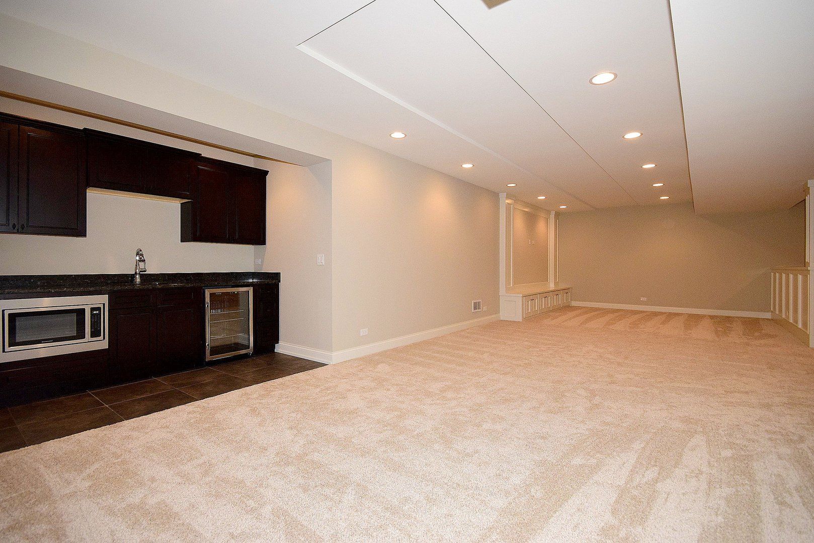 An empty basement with a kitchen and a refrigerator