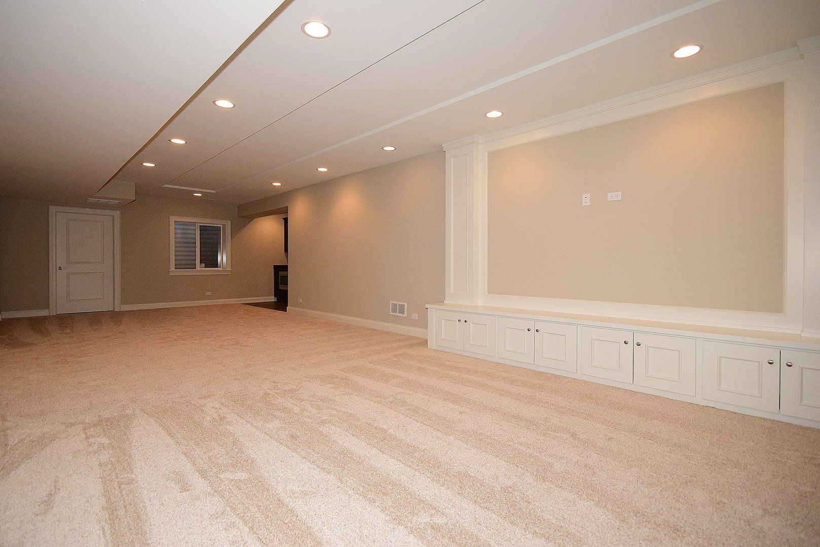 An empty basement with a carpeted floor and a large wall.