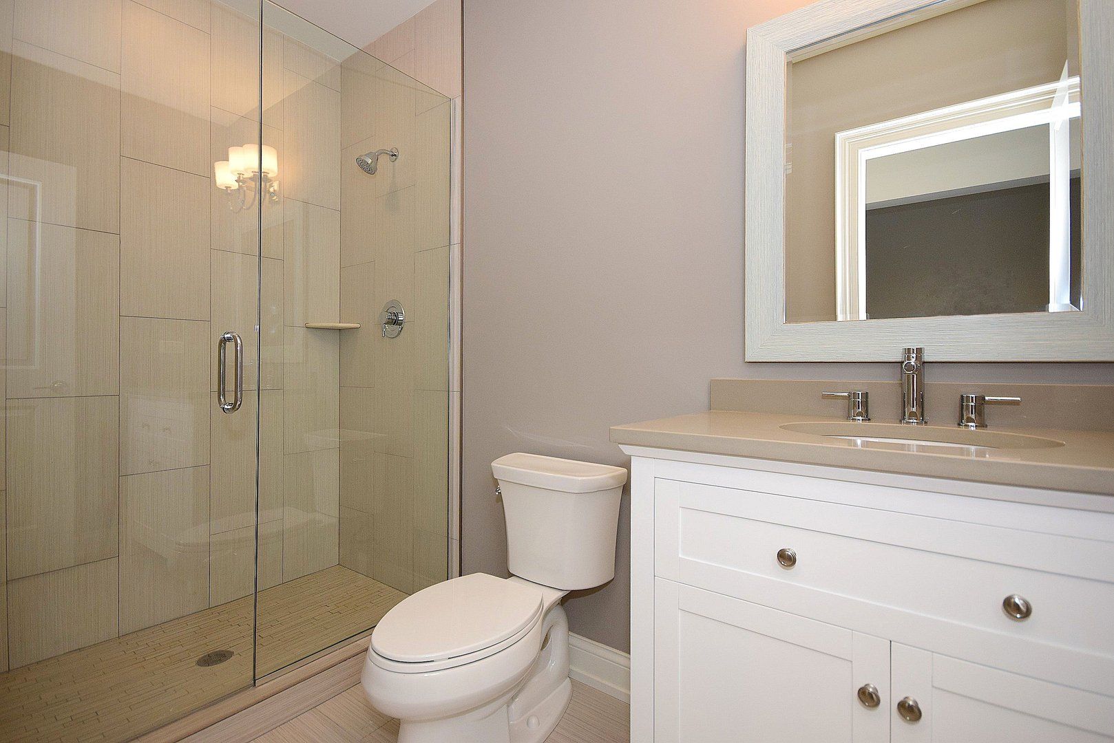 A bathroom with a toilet , sink , mirror and walk in shower.