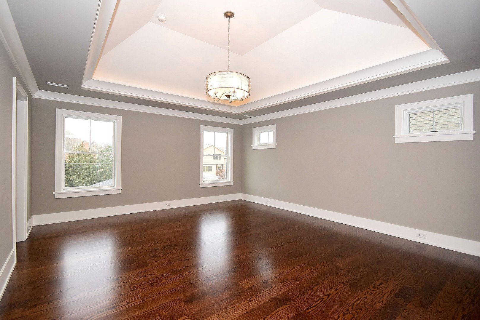An empty room with hardwood floors and a chandelier hanging from the ceiling.