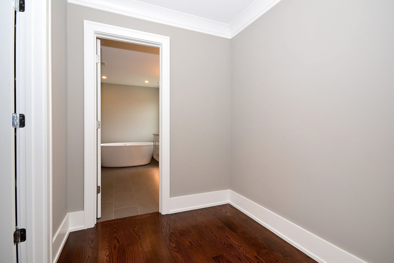 An empty room with hardwood floors and a door leading to a bathroom.