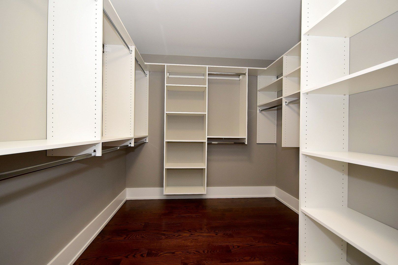 An empty walk in closet with white shelves and wooden floors.