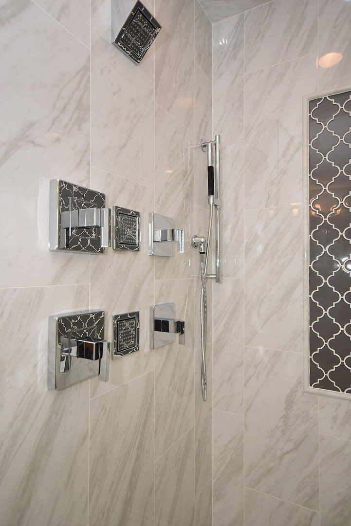 A close up of a shower head in a bathroom with marble tiles.