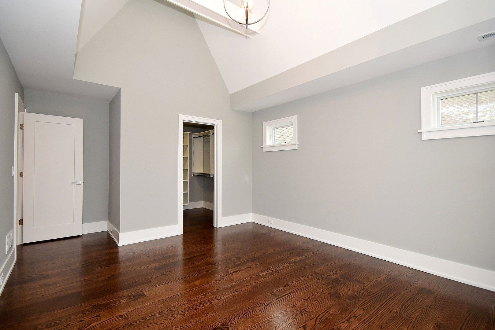 An empty room with hardwood floors and a vaulted ceiling.