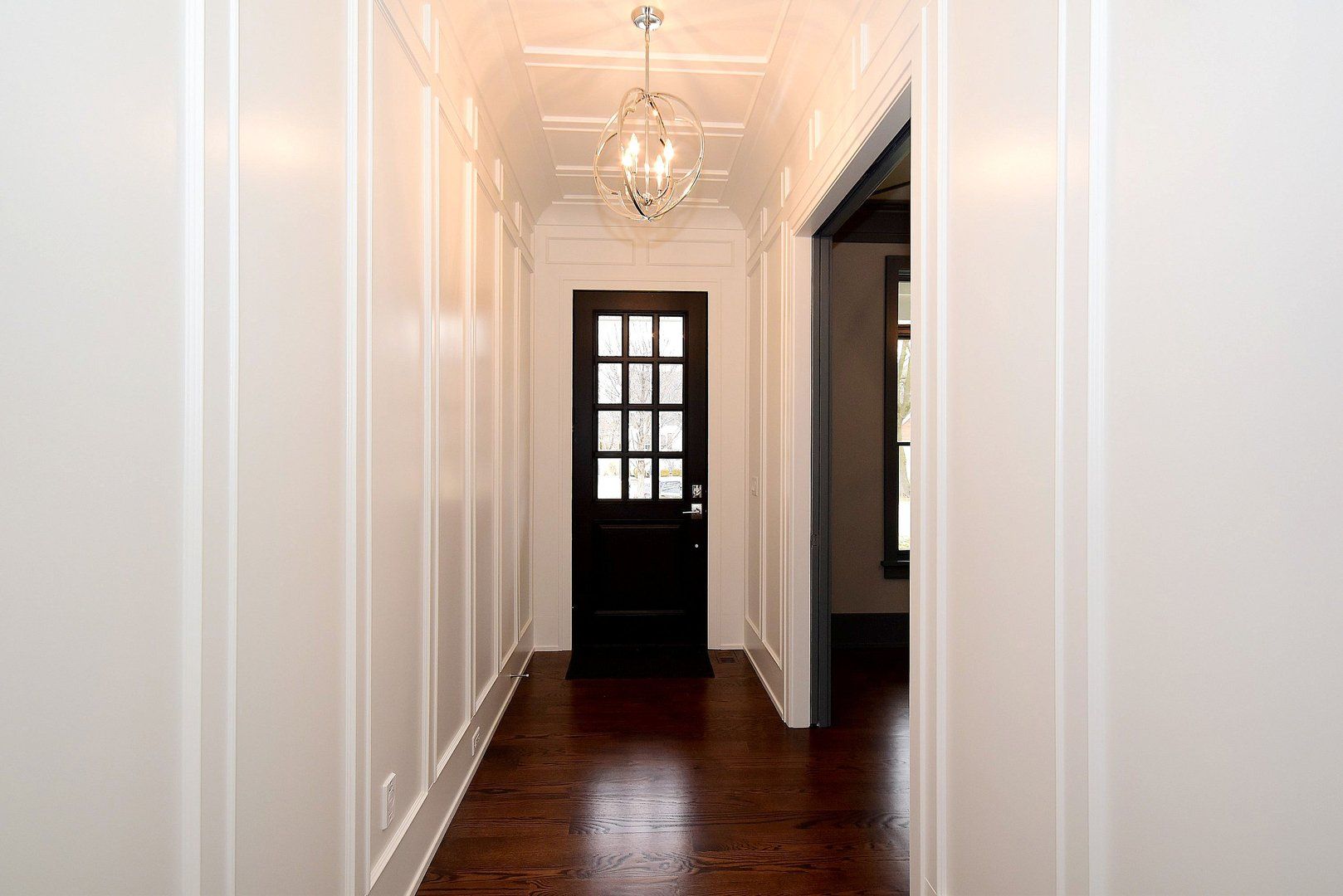 A long hallway with a black door and a chandelier hanging from the ceiling.