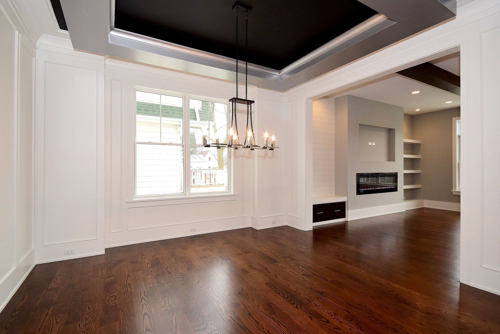 An empty living room with hardwood floors and a chandelier hanging from the ceiling.