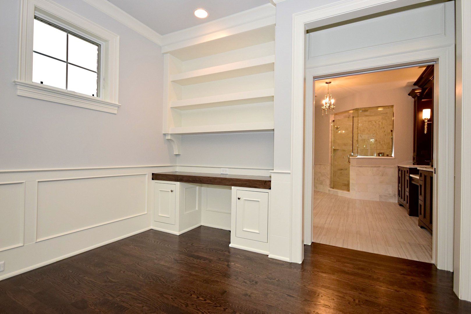 An empty room with a desk and shelves next to a bathroom.