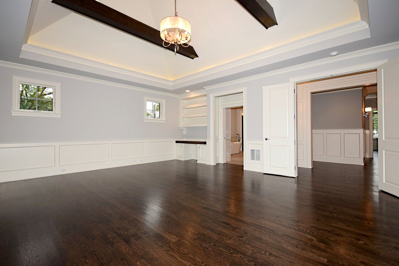 An empty room with hardwood floors and a chandelier hanging from the ceiling