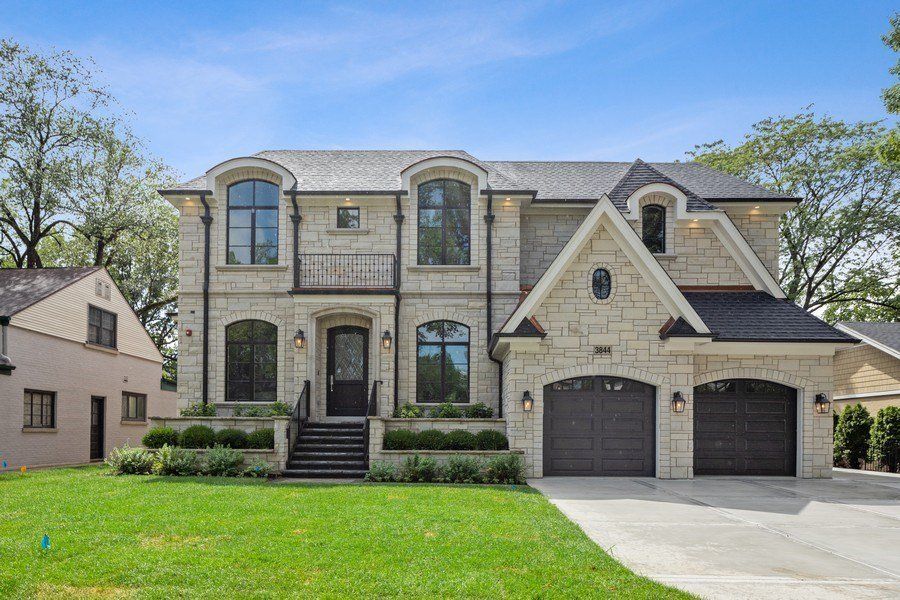 A large brick house with two garages and a large lawn in front of it.