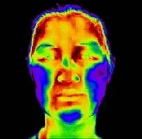 Thermal image of a face, showing heat distribution. Warmer areas appear yellow/red, cooler areas blue/purple.