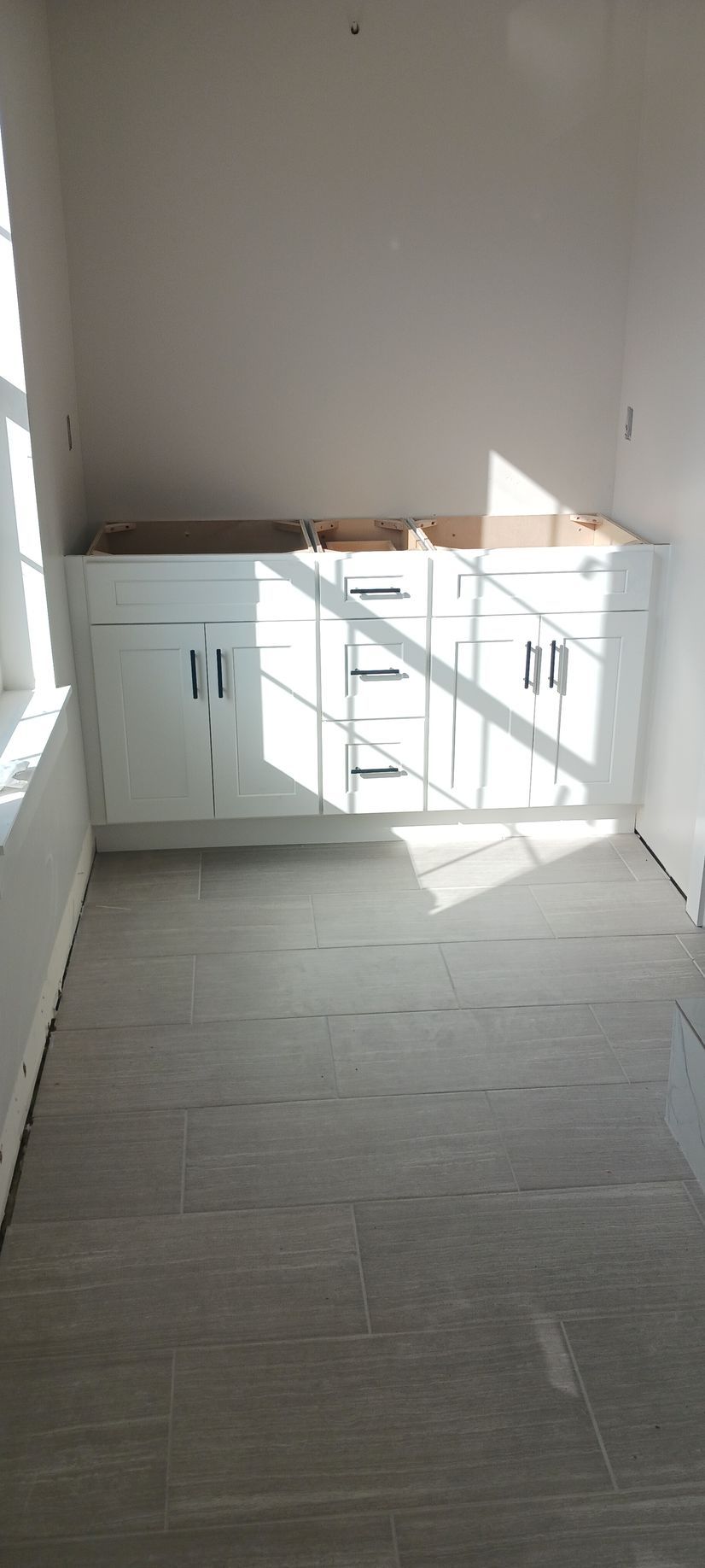 A kitchen under construction with white cabinets and a tiled floor.