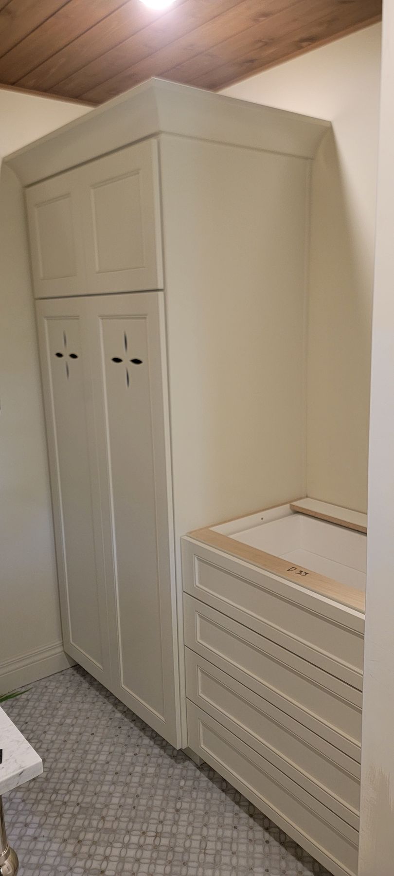 A laundry room with white cabinets and drawers and a wooden ceiling.
