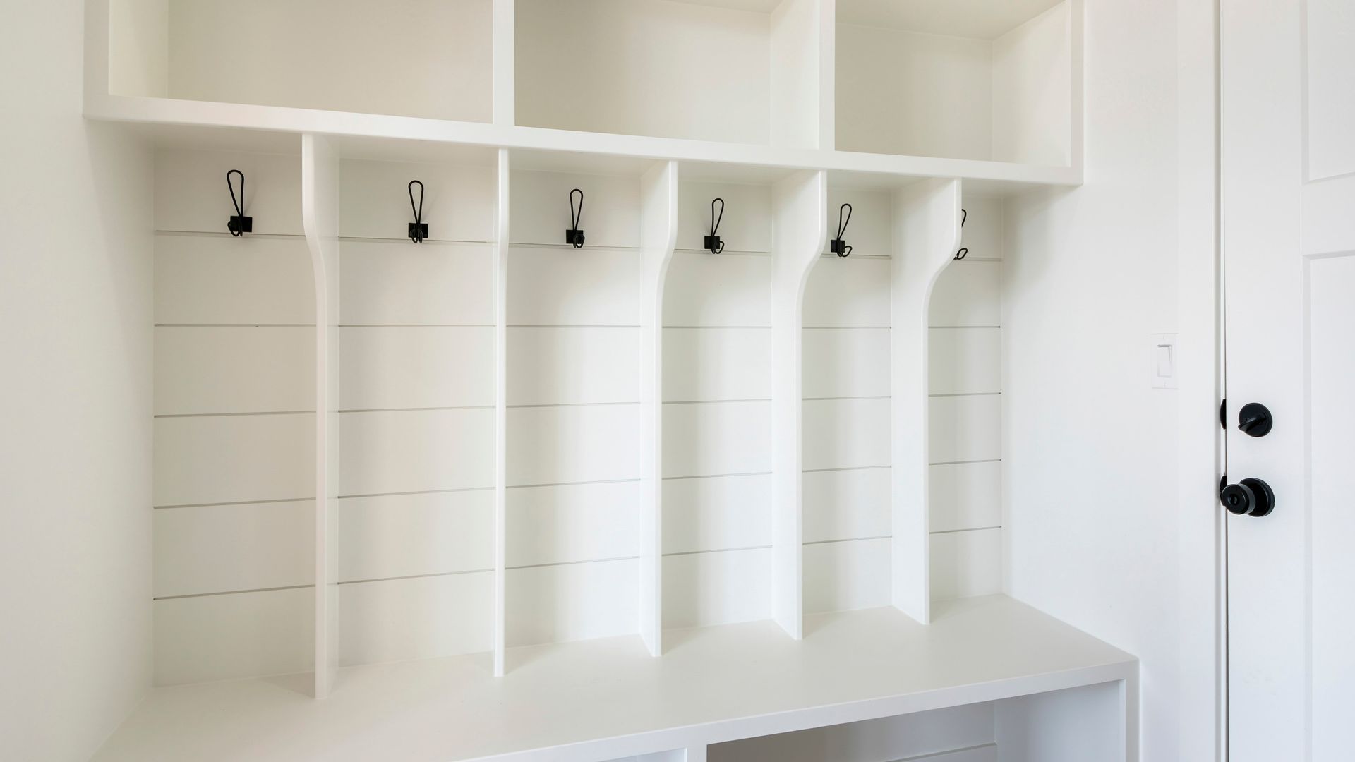 White built-in locker unit with open shelves, hooks, and a bench. Located inside a home near a door.