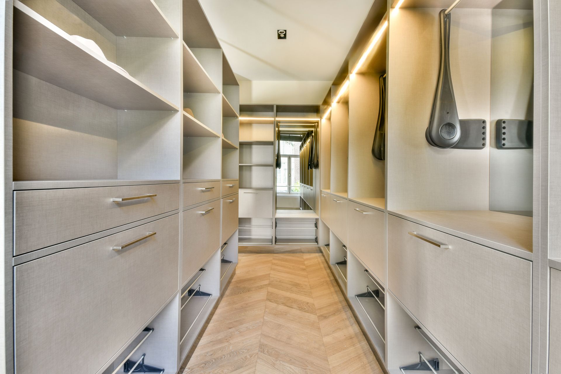 Walk-in closet with beige shelving, drawers, and herringbone wood floor.