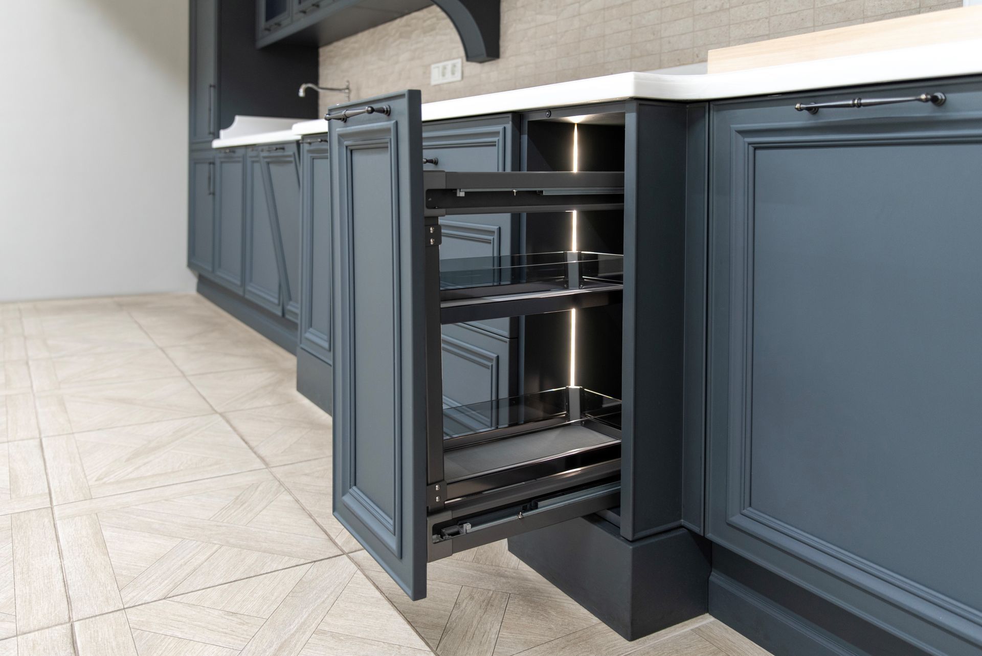 A pull-out pantry cabinet drawer in a modern kitchen with navy blue cabinetry and white countertops.
