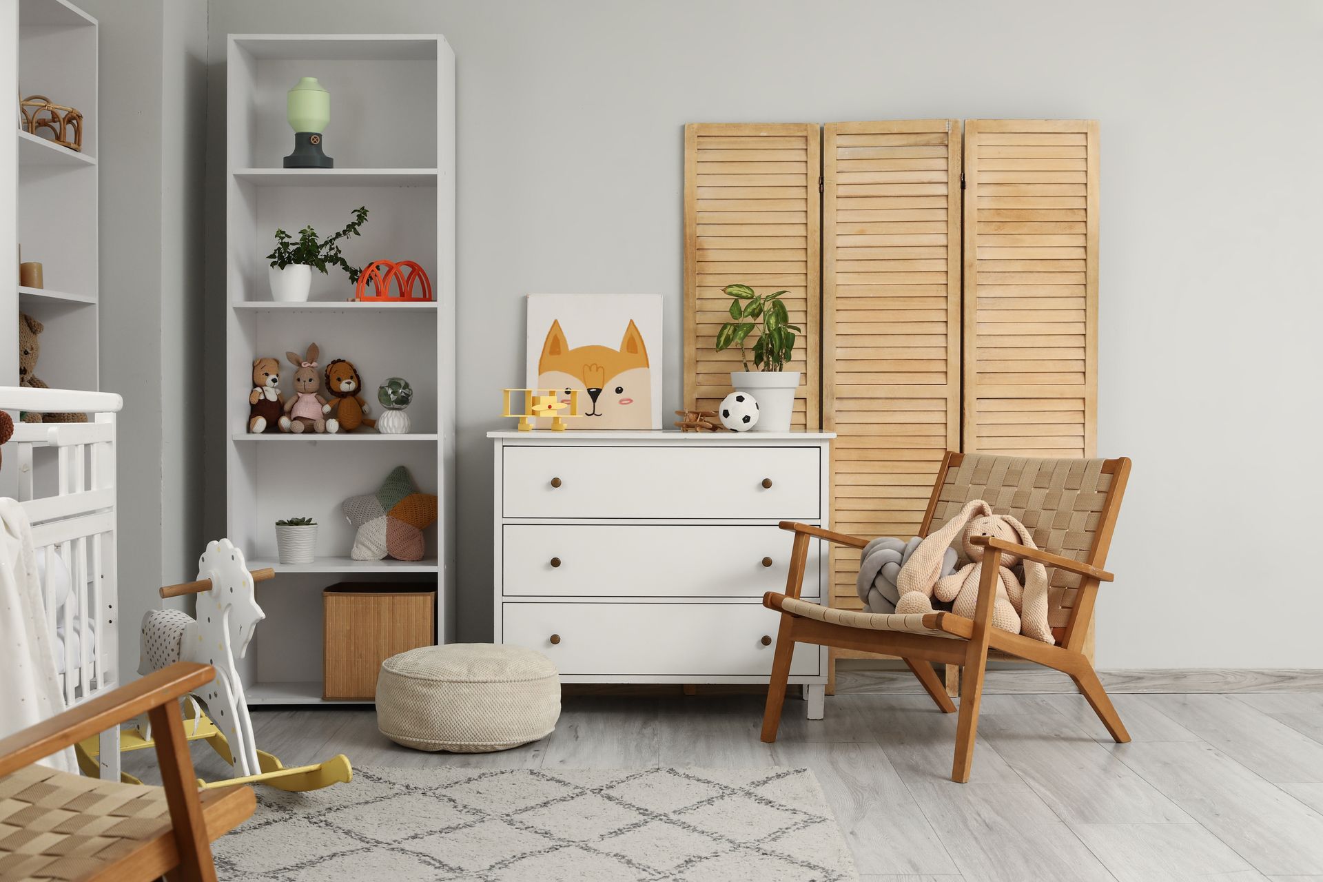 A nursery with a white dresser, bookshelf, wooden folding screen, rocking chair, and a stuffed toy fox print on the wall.