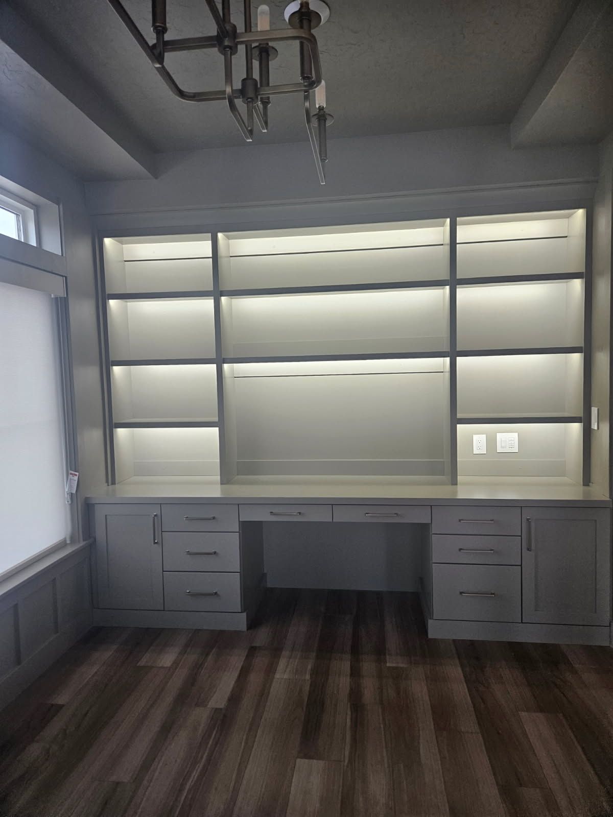 A room with a desk , shelves , drawers and a chandelier.