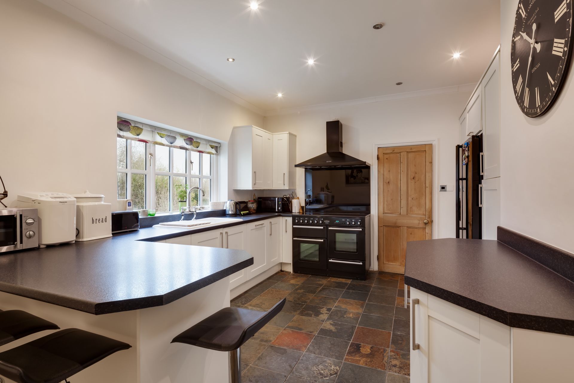 A kitchen with white cabinets and black counter tops and a clock on the wall.
