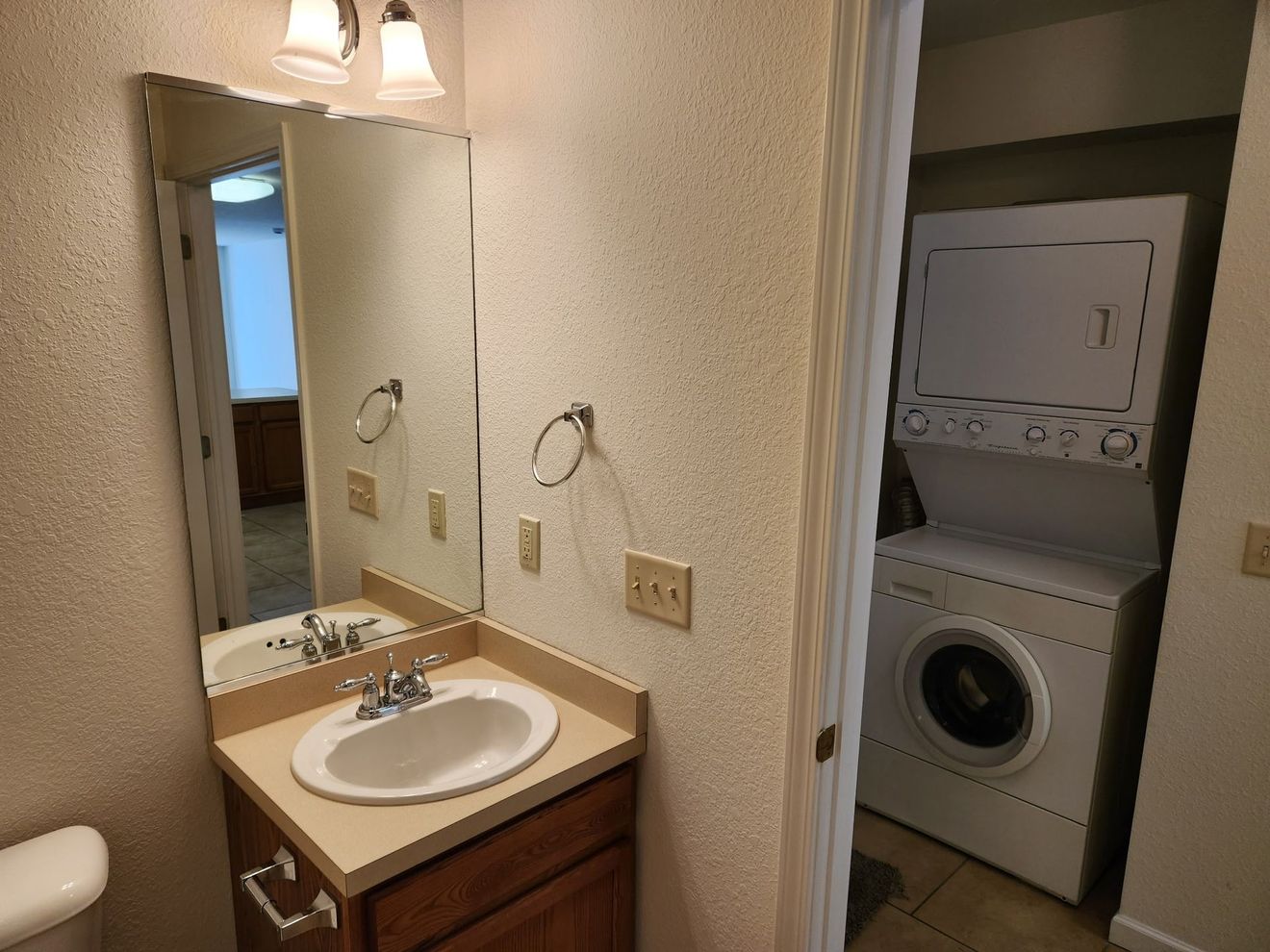 Bathroom vanity with mirror next to an open laundry closet with stacked washer and dryer