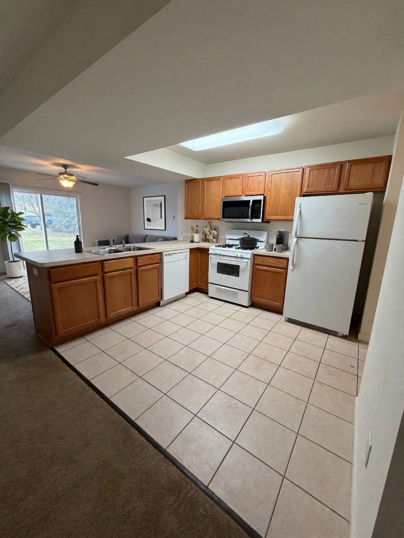 Bright kitchen with white appliances, wood cabinets, tiled floor, and a window over the sink