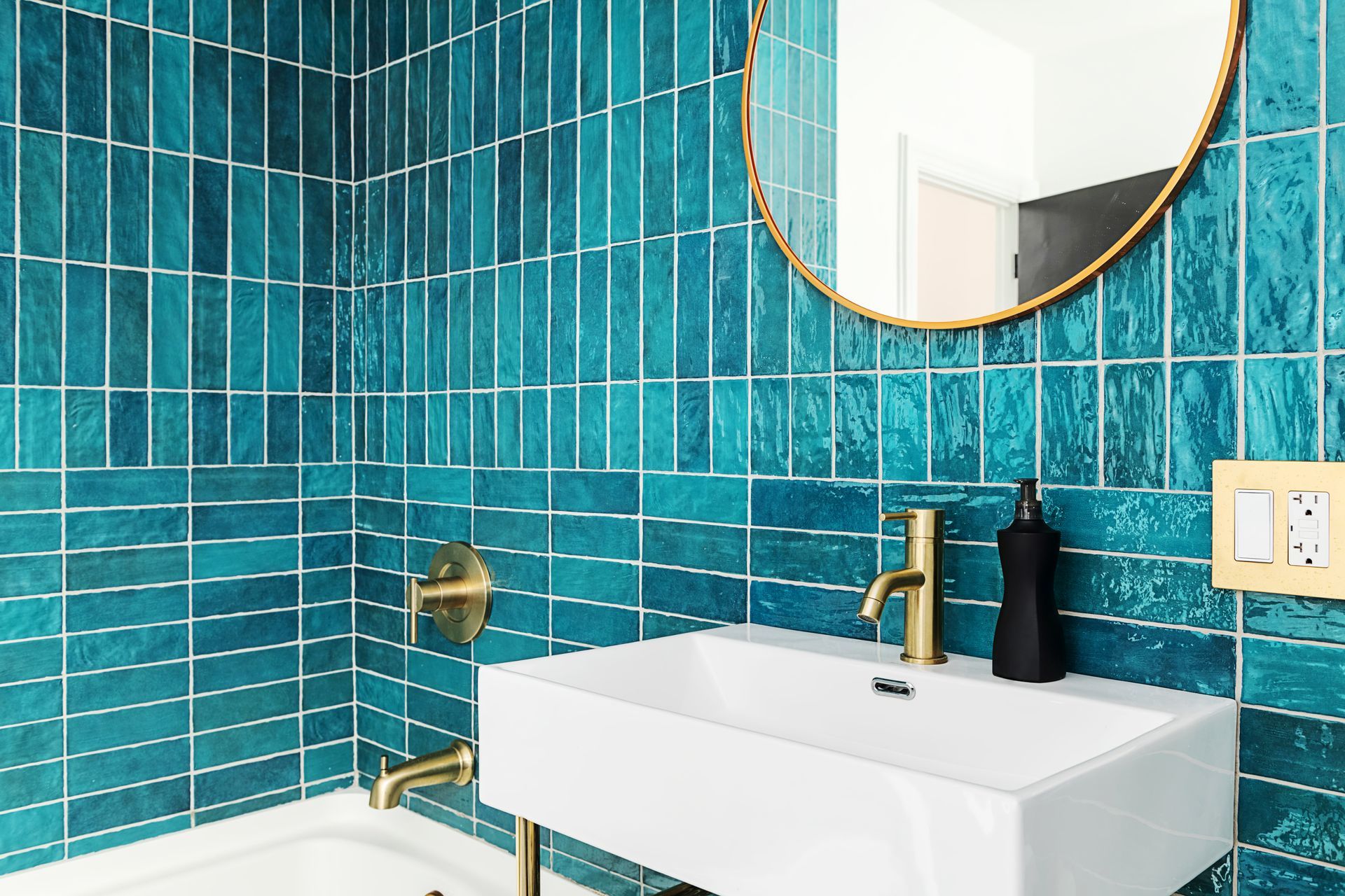 A bathroom with blue tiles , a sink , a mirror and a bathtub.