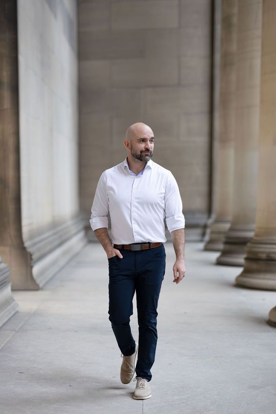 Man in a white shirt and dark jeans walking through a columned stone corridor