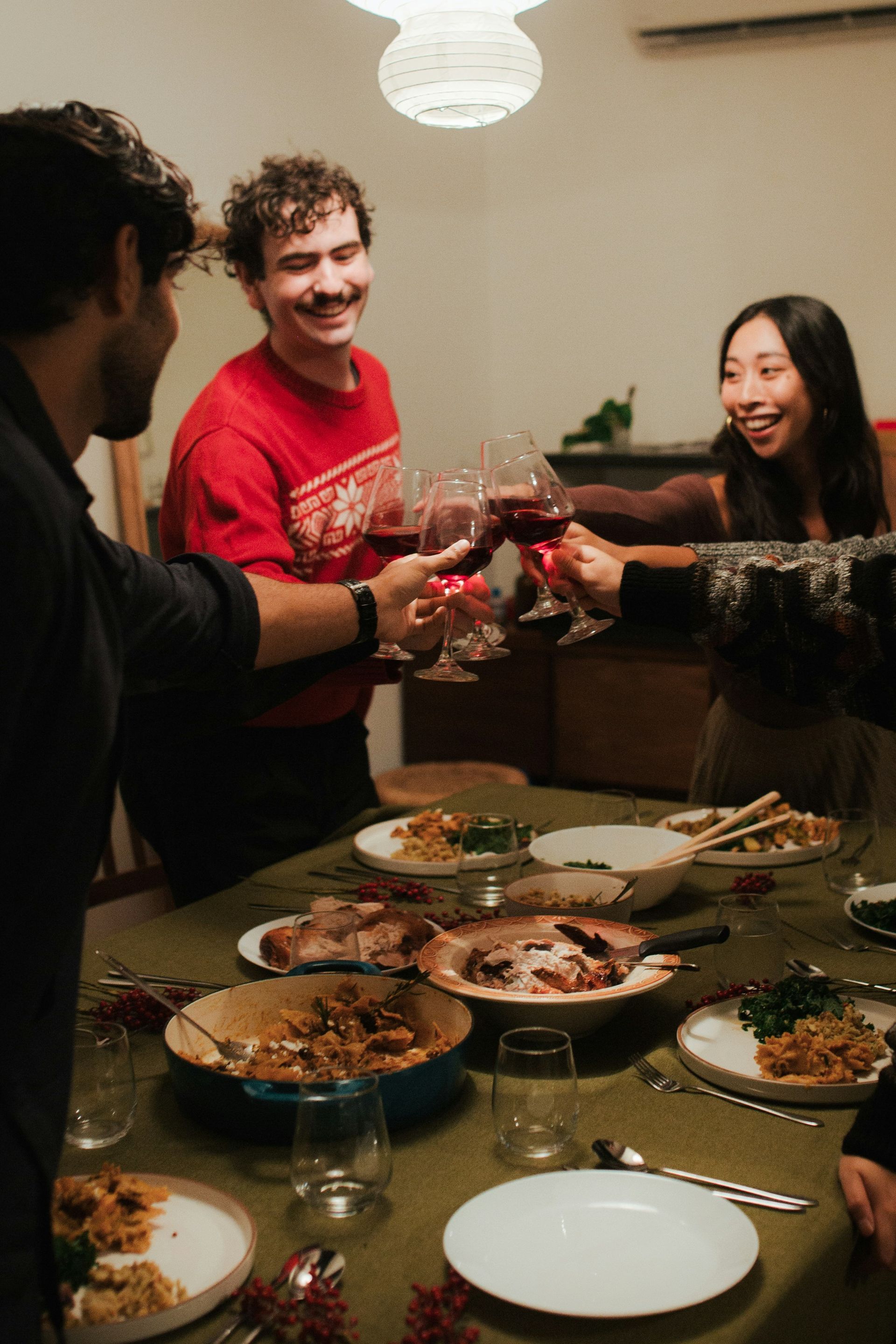 Friends toasting with wine glasses around a dinner table with shared dishes in a cozy dining room.