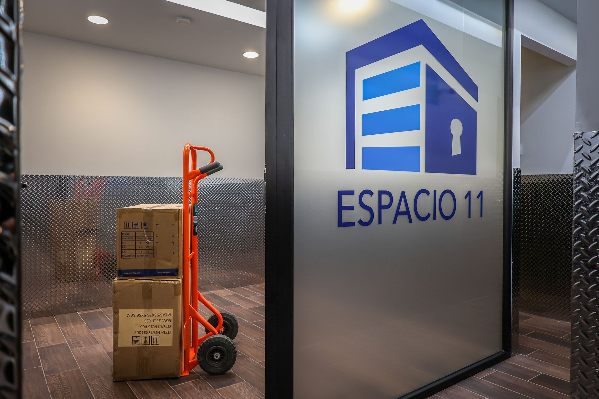 Interior de unidad de almacenamiento con cajas en una carretilla manual, logotipo en la puerta.