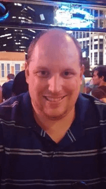 A bald man in a blue shirt is smiling for the camera.