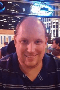 A man with a bald head is smiling and wearing a blue shirt.