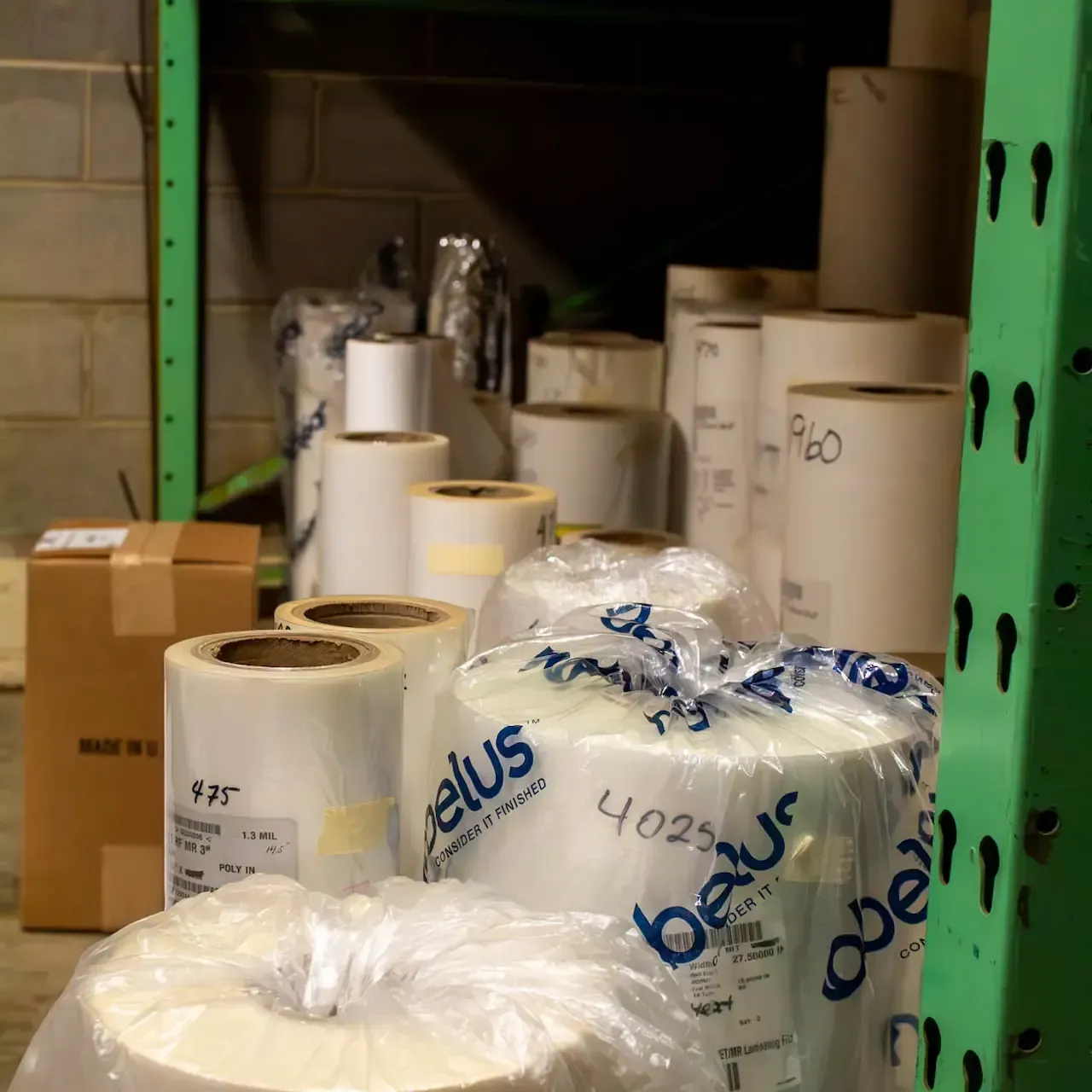 Rolls of clear plastic film, some labeled with numbers, in a warehouse setting.