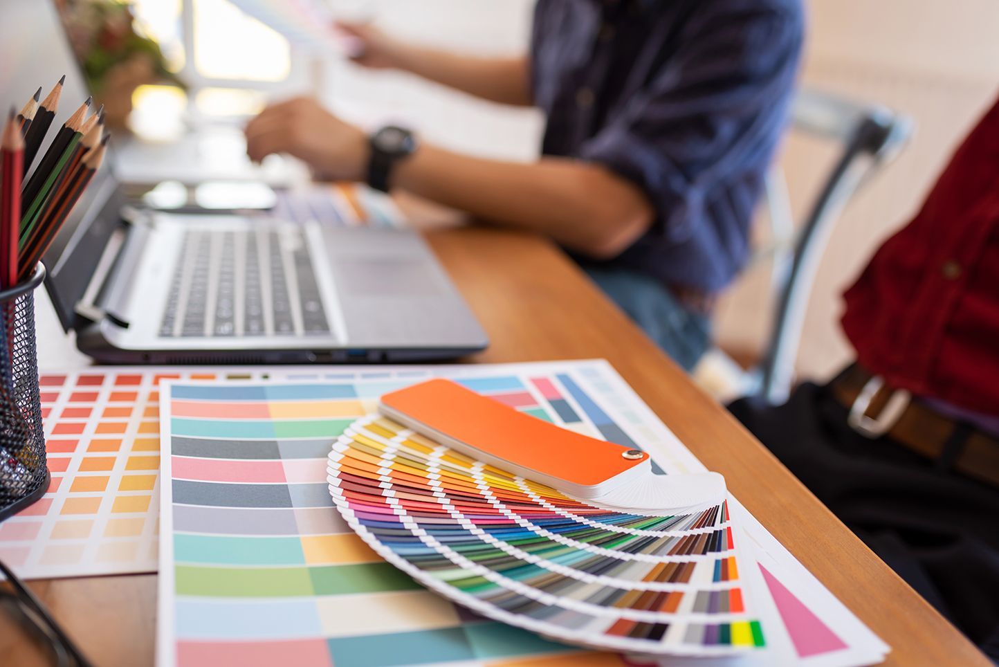 A person is sitting at a desk with a laptop and a color palette.