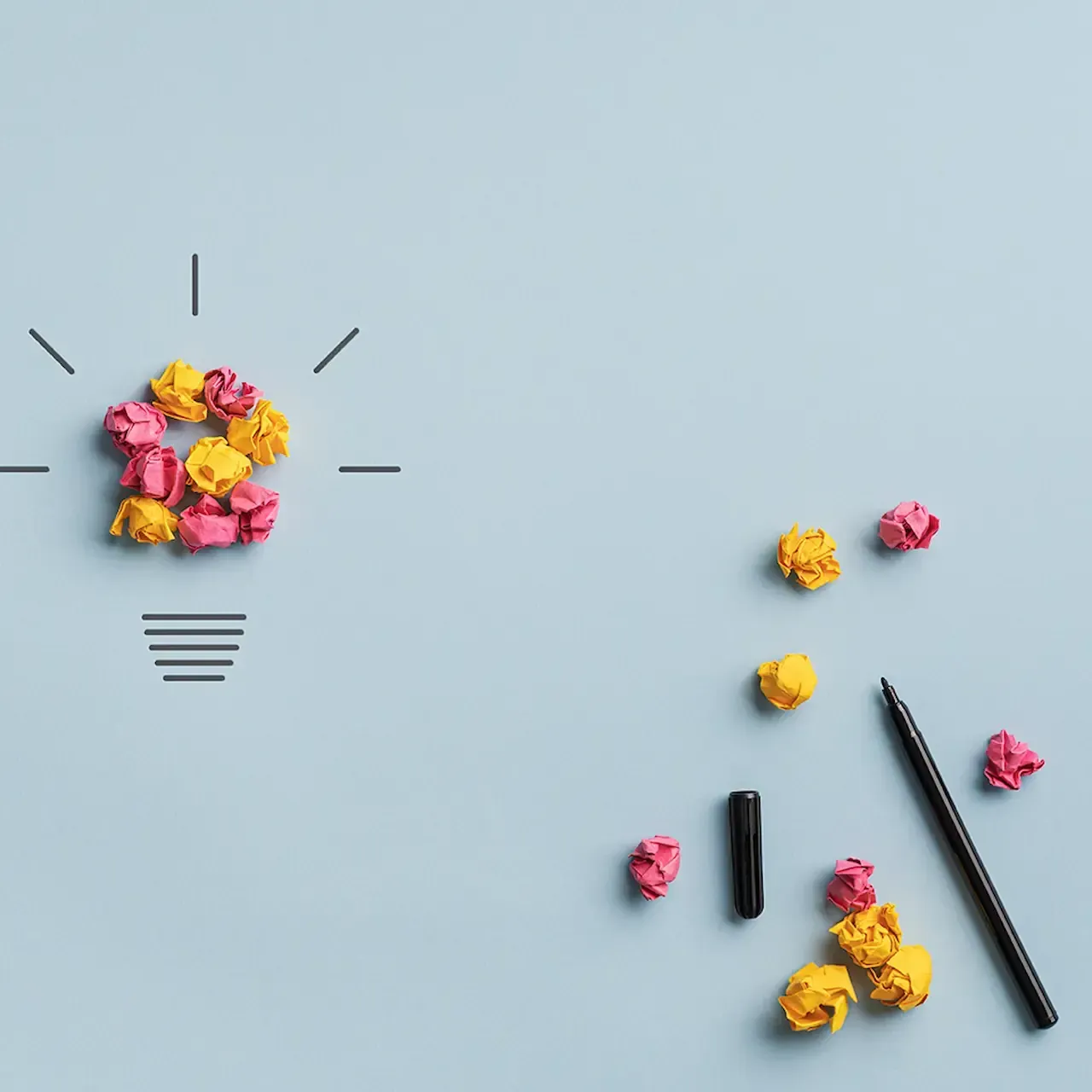 Light bulb made of crumpled paper, with drawn lines and scattered paper, pen on a blue background.