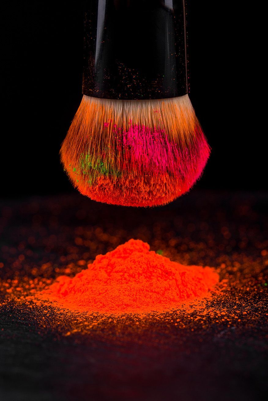 A close up of a makeup brush with colored powder coming out of it.