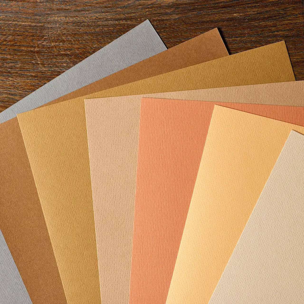 Paper finishes guide: assorted paper finish types including gloss, matte, satin, and textured finishes fanned out on a wood surface