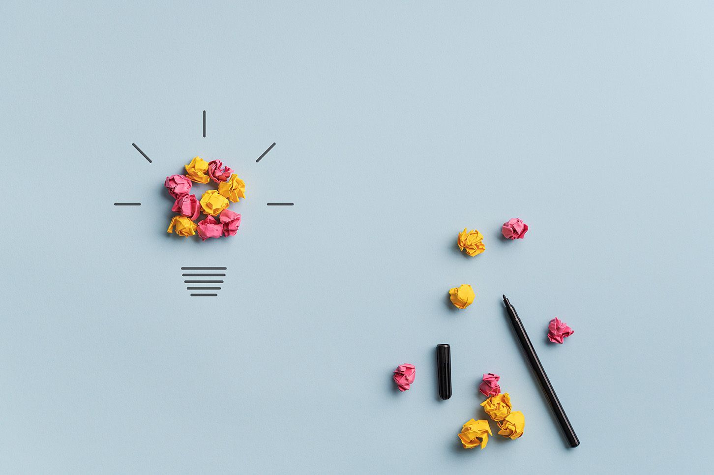 A light bulb made of crumpled paper and pencils on a blue background.