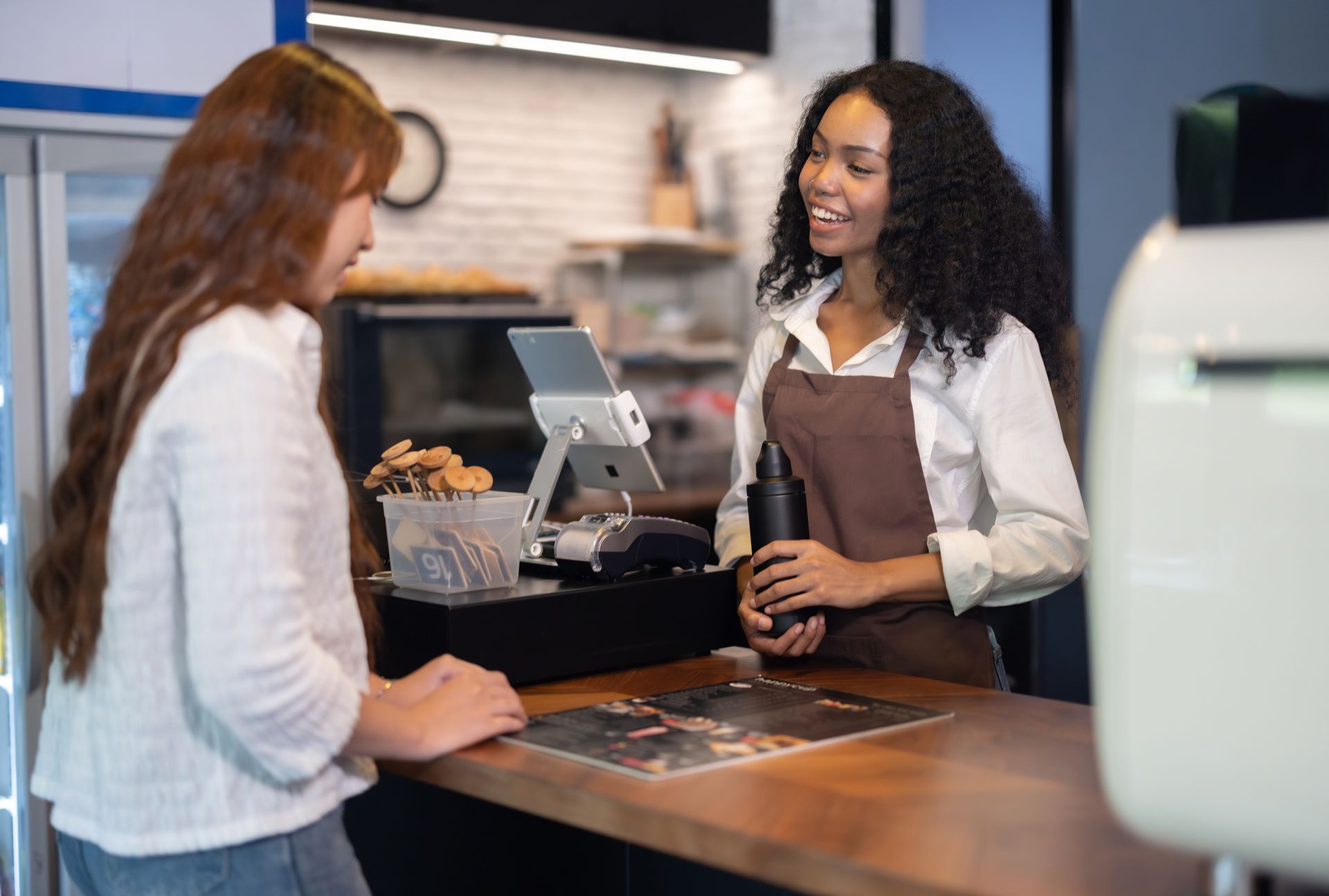 A woman is standing at a counter in a restaurant talking to a customer.