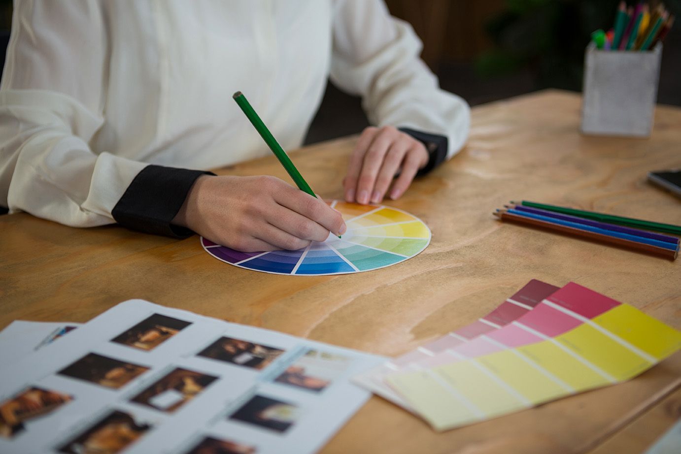 A woman is sitting at a table drawing on a color wheel with a pencil.