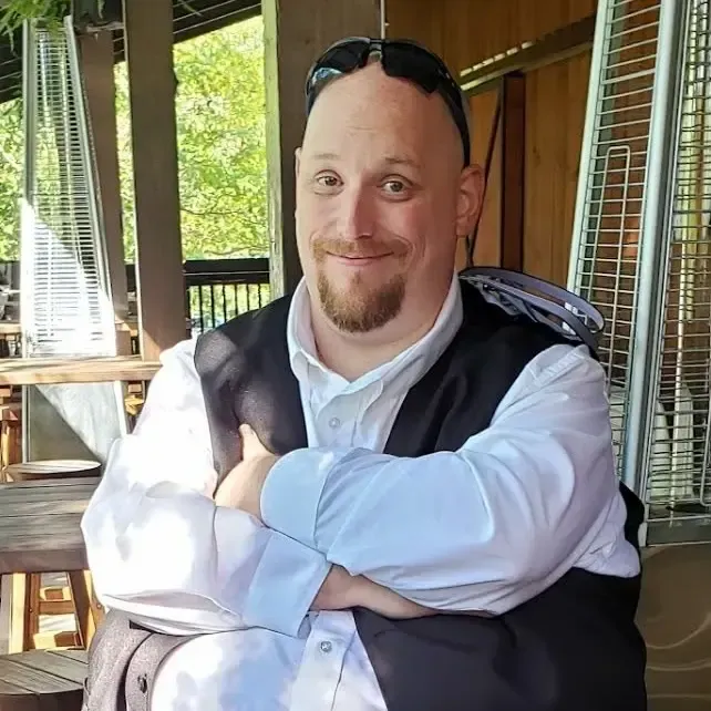 Man smiling in a blue striped shirt; city lights in the background.