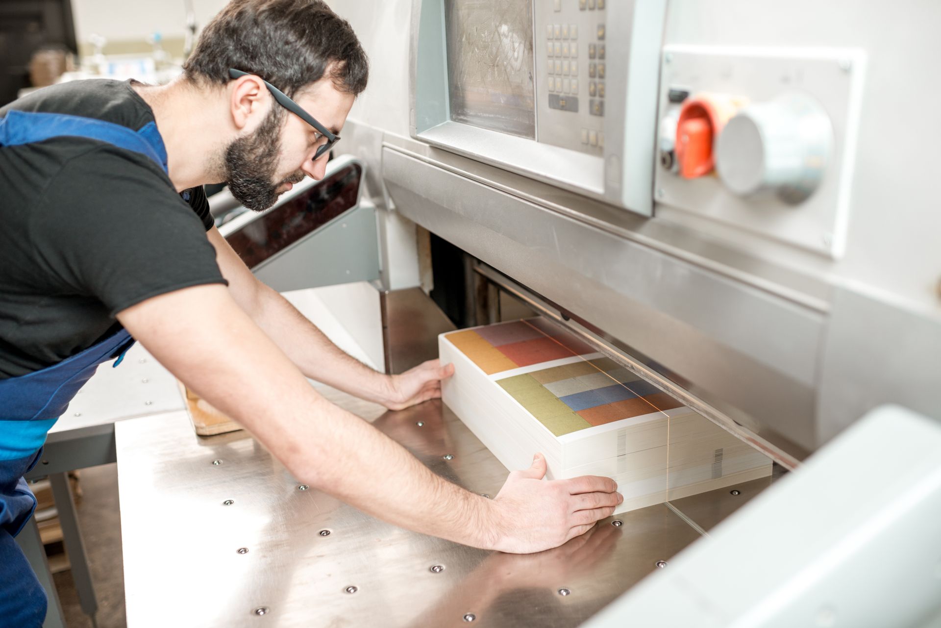 Man using a paper cutter to trim a stack of printed material, indoors.