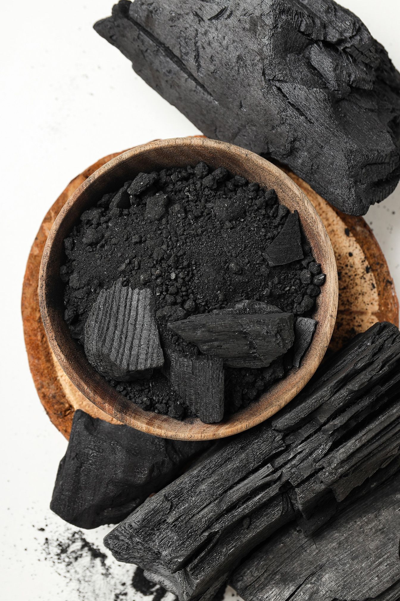 A wooden bowl filled with black charcoal is surrounded by pieces of charcoal.