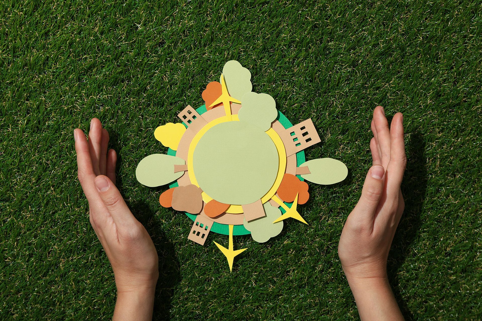 A person is holding a paper cut out of a globe on the grass.