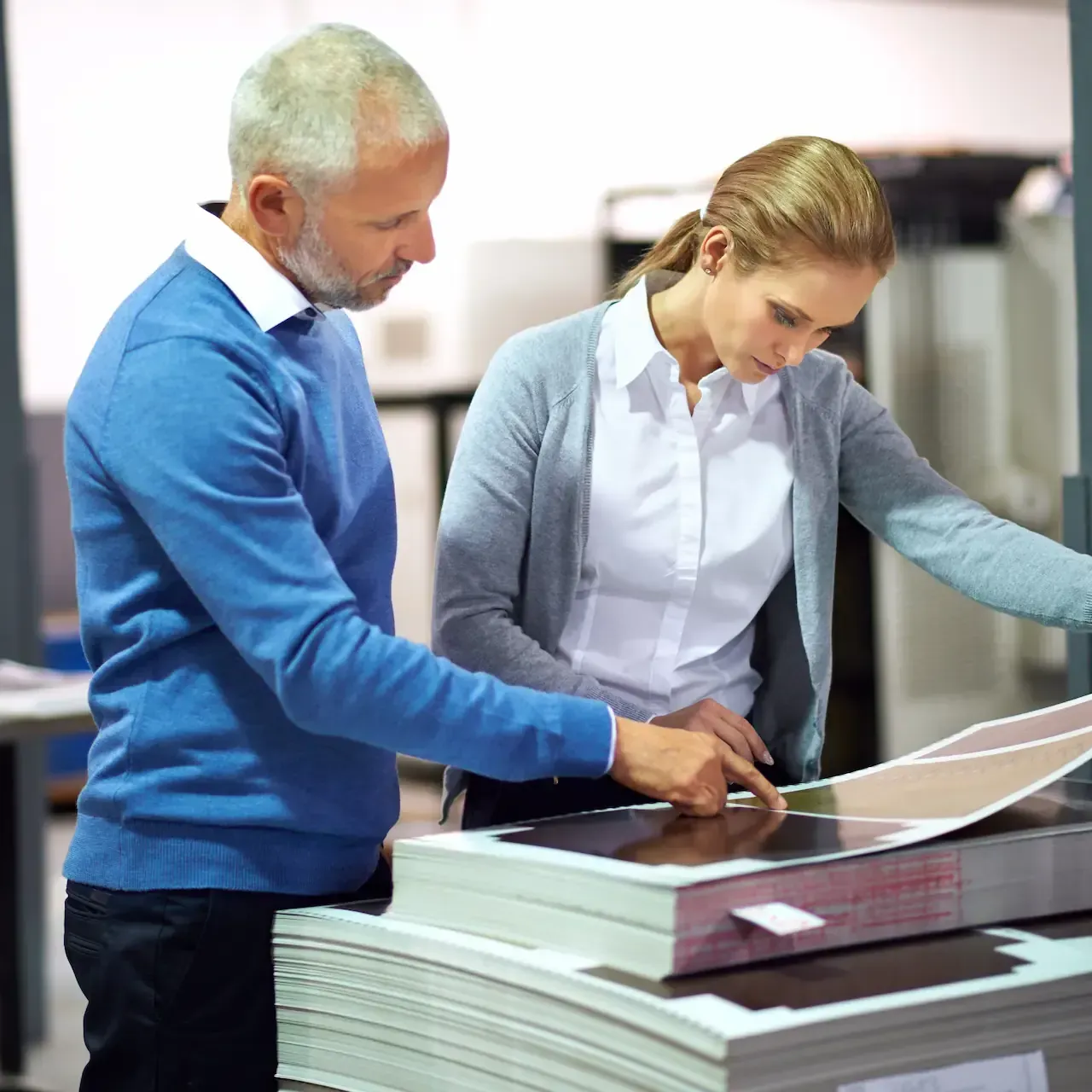 Man and woman examining printed materials near a printing machine.