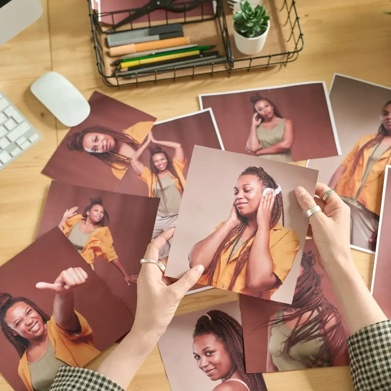 Hands holding a photo of a woman with braided hair surrounded by other photos on a desk.