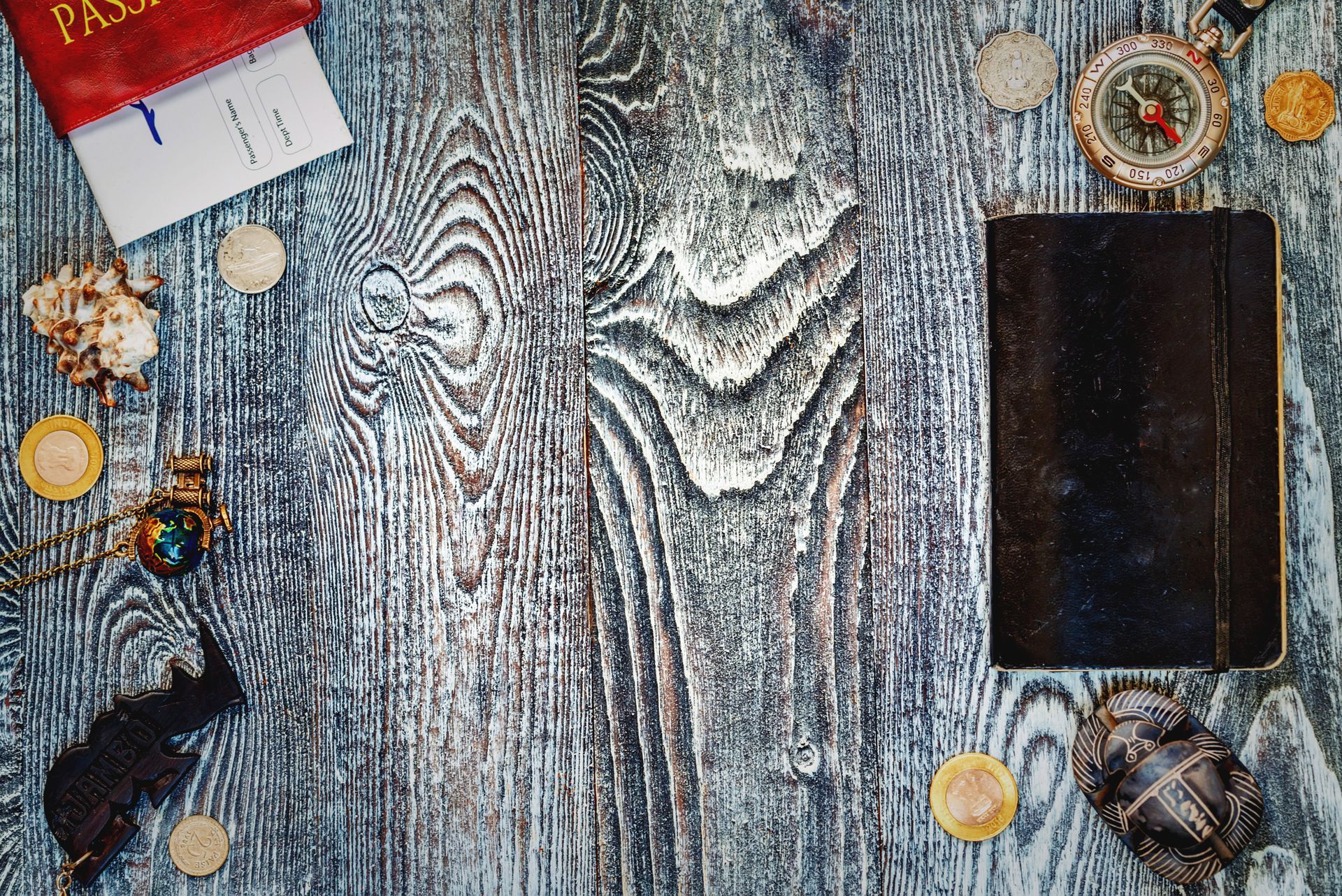 A wooden table topped with a passport , book , compass , and seashells.