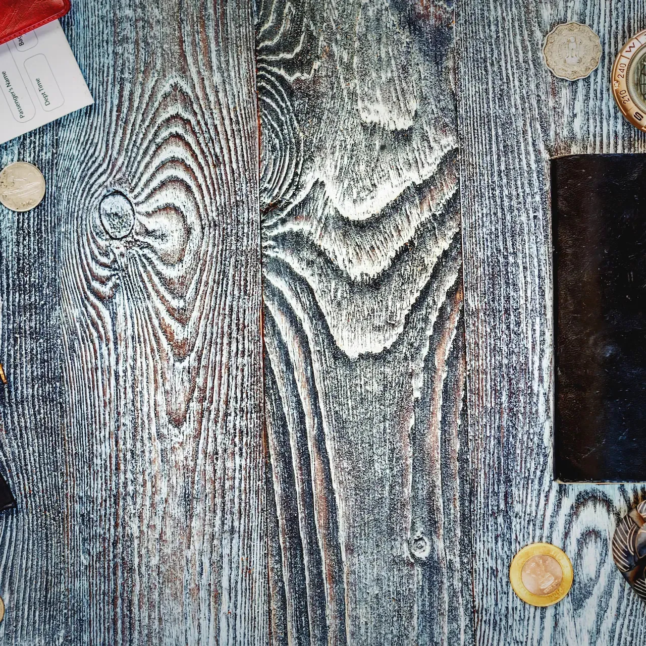 Passport, compass, book, shells, coins, and travel trinkets on a weathered wood surface.