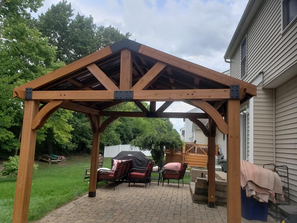 A wooden gazebo is sitting in the backyard of a house.
